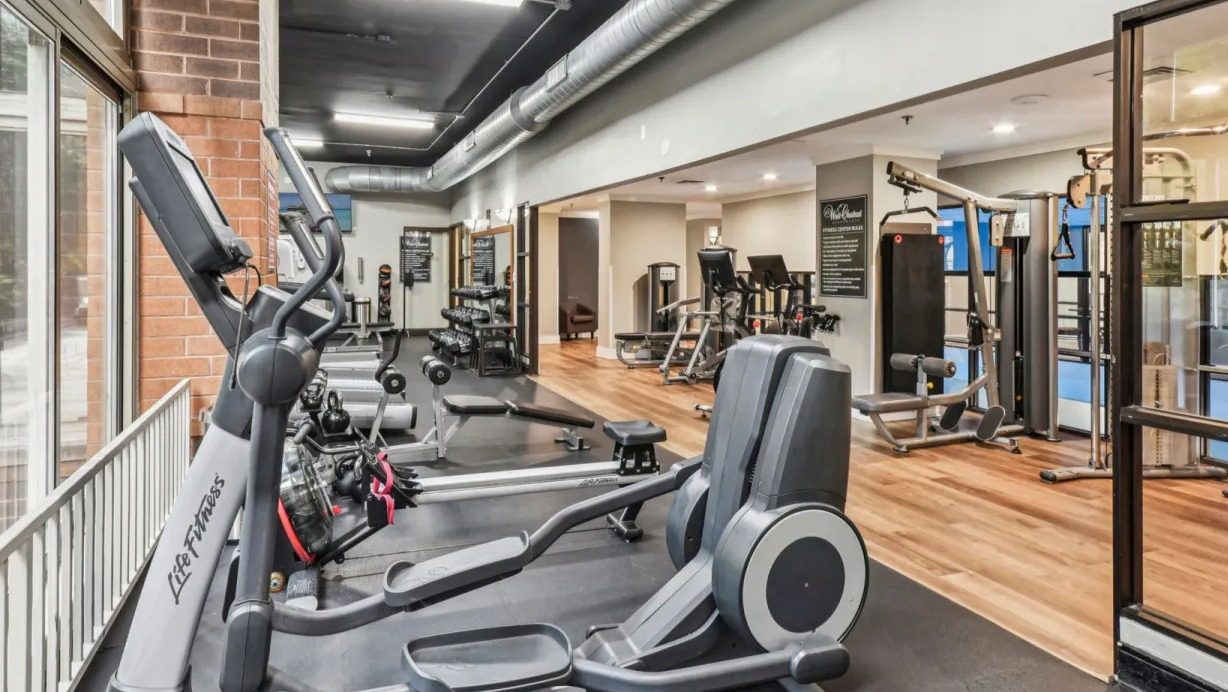 Fitness center at 100 W Chestnut in Chicago with cardio machines, weight training equipment, mirrored walls, and large windows for natural light