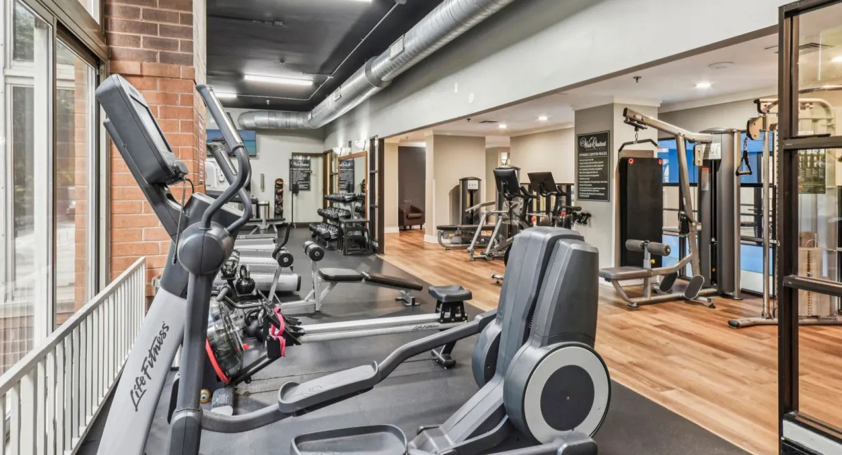 Fitness center at 100 W Chestnut in Chicago with cardio machines, weight training equipment, mirrored walls, and large windows for natural light