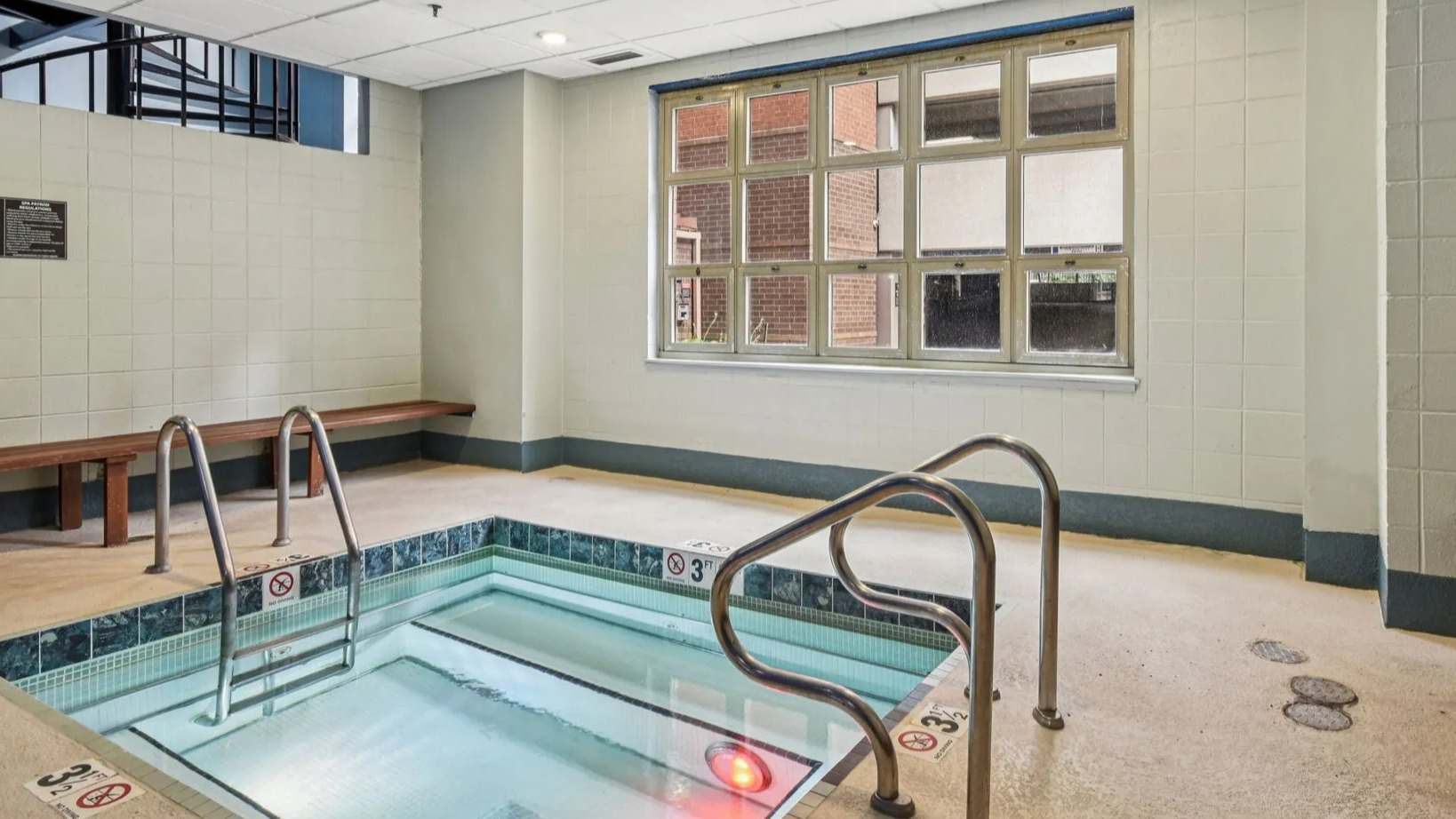 Indoor hot tub at 100 W Chestnut in Chicago with tiled surround, handrails, bench seating, and warm lighting for relaxing after work or workouts