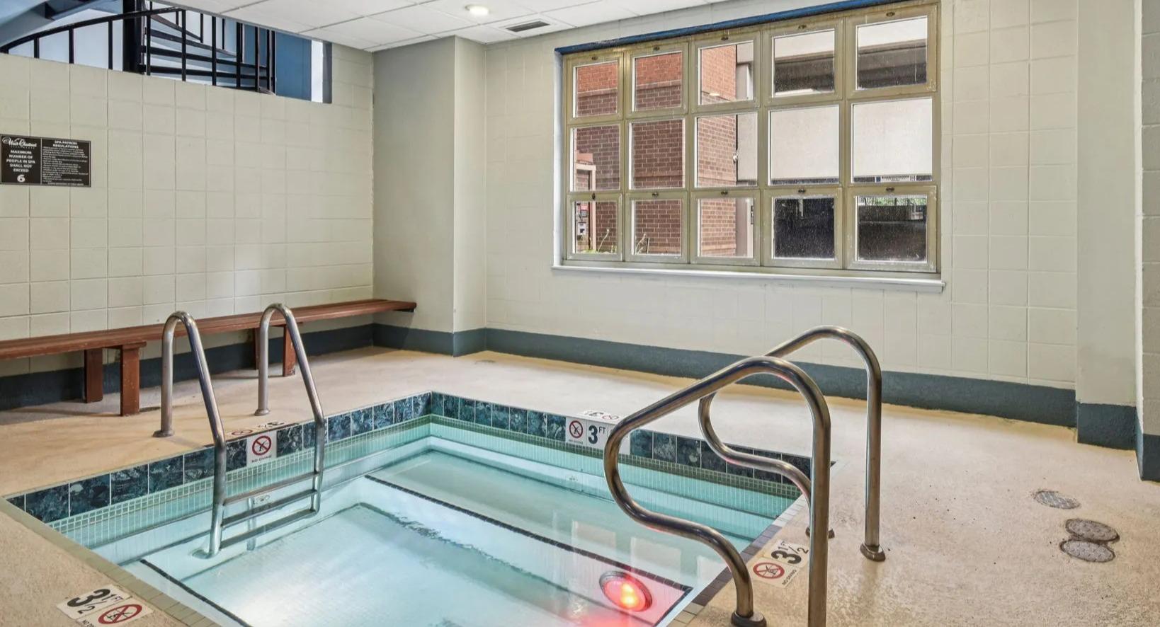 Indoor hot tub at 100 W Chestnut in Chicago with tiled surround, handrails, bench seating, and warm lighting for relaxing after work or workouts