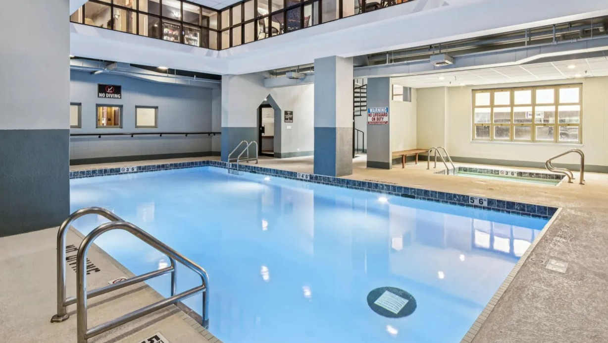 Indoor pool and hot tub at 100 W Chestnut in Chicago featuring lap lanes, tiled deck, whirlpool spa, and bright overhead lighting