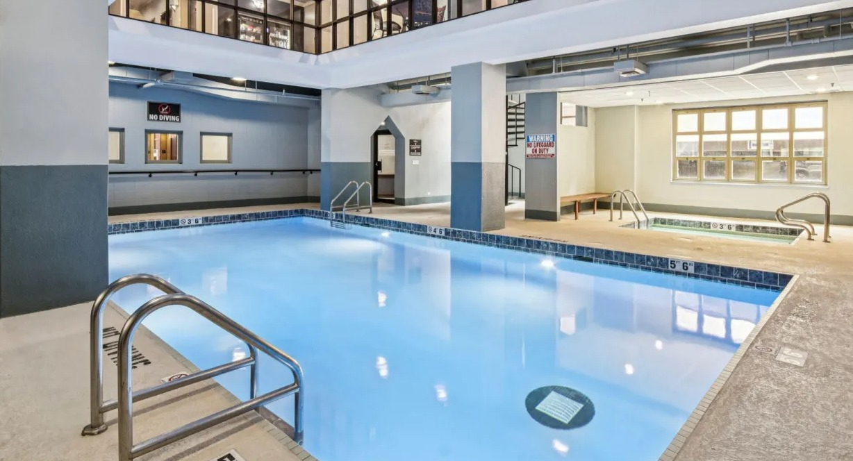 Indoor pool and hot tub at 100 W Chestnut in Chicago featuring lap lanes, tiled deck, whirlpool spa, and bright overhead lighting