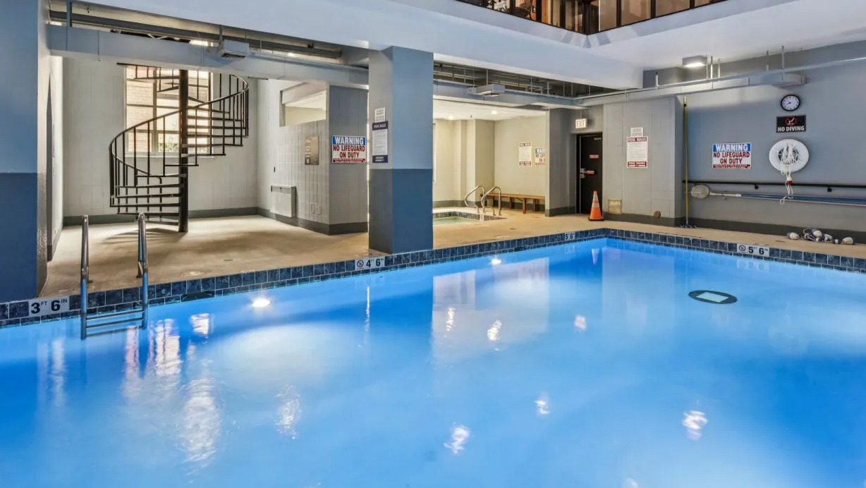 Modern indoor swimming pool at 100 W Chestnut in Chicago with spiral staircase, lounge seating, and glass-walled second floor overlooking the pool