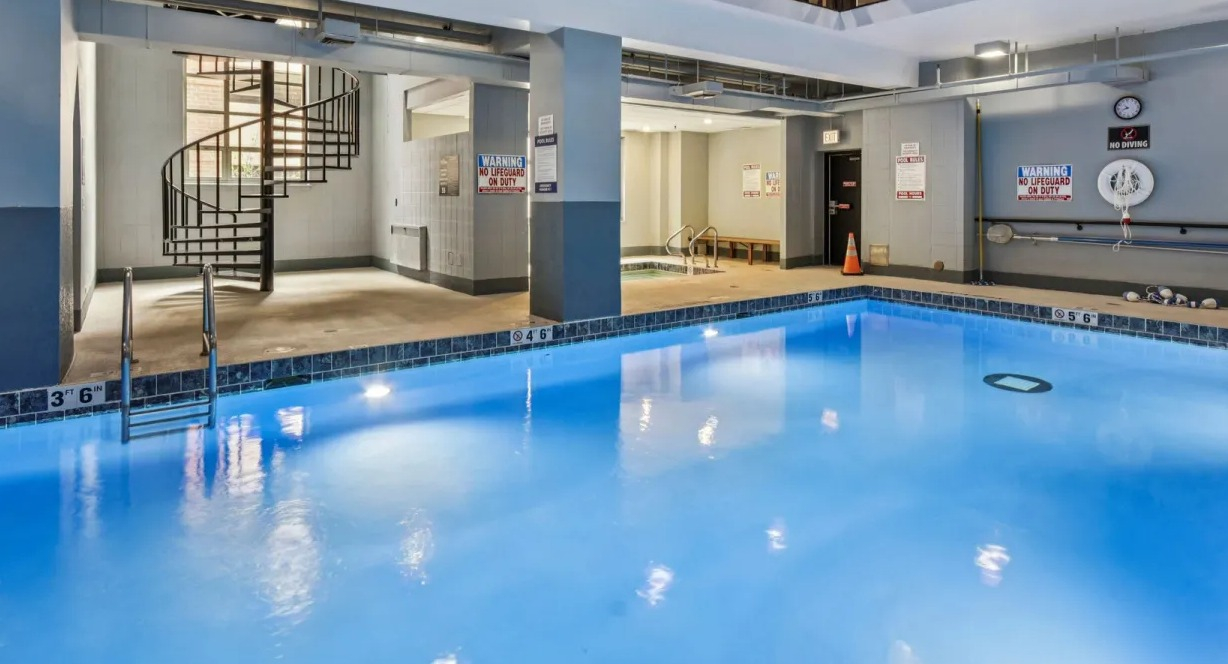 Modern indoor swimming pool at 100 W Chestnut in Chicago with spiral staircase, lounge seating, and glass-walled second floor overlooking the pool