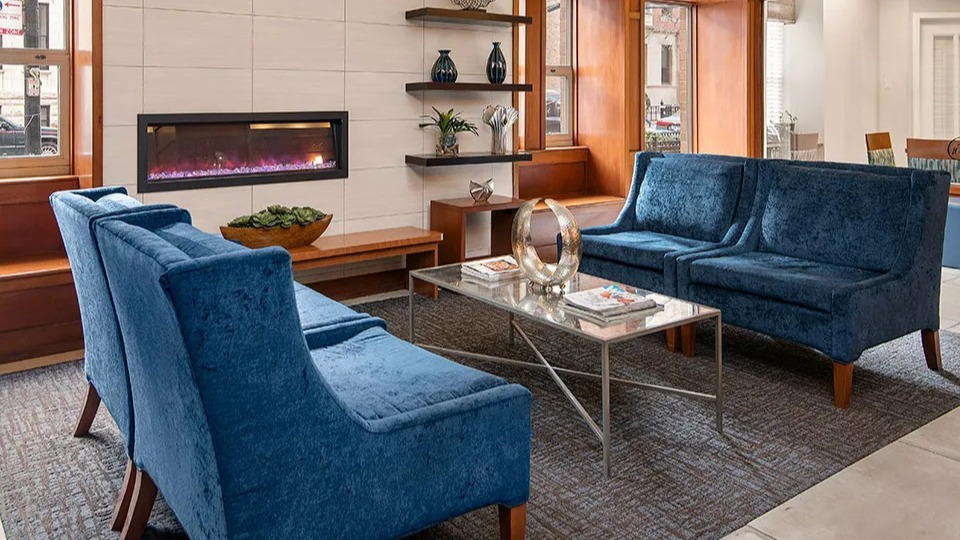 Inviting lobby at 100 W Chestnut in Chicago featuring a modern linear fireplace, blue velvet seating, built-in shelving, and warm wood details