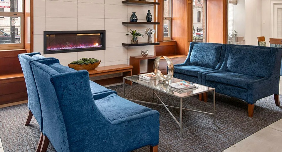Inviting lobby at 100 W Chestnut in Chicago featuring a modern linear fireplace, blue velvet seating, built-in shelving, and warm wood details