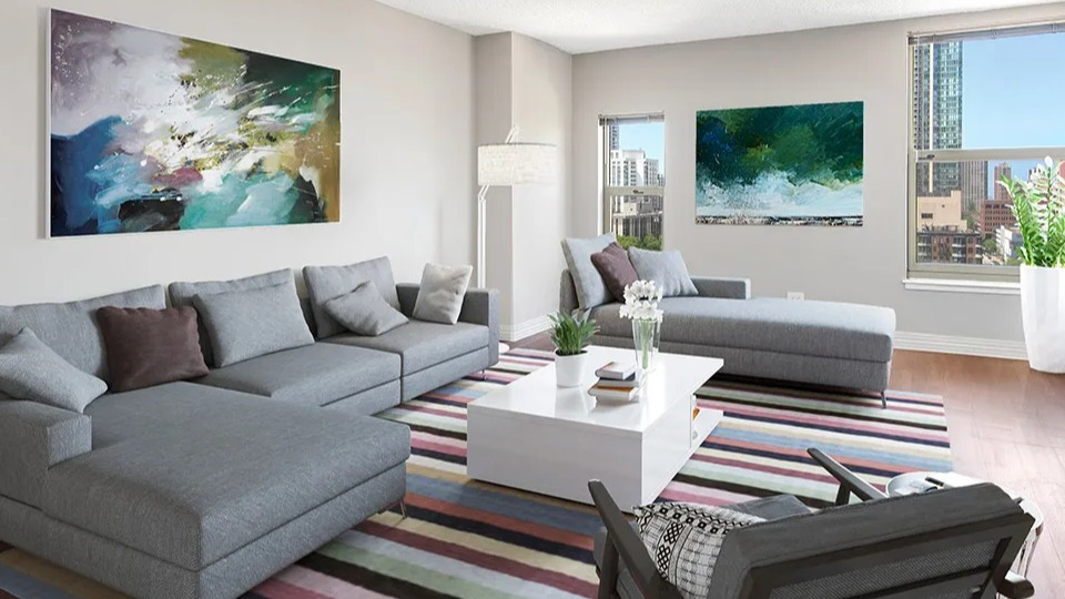 Modern living room at 100 W Chestnut in Chicago with sectional sofa, colorful striped rug, large artwork, and multiple windows offering natural light