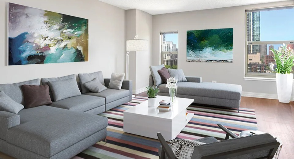 Modern living room at 100 W Chestnut in Chicago with sectional sofa, colorful striped rug, large artwork, and multiple windows offering natural light