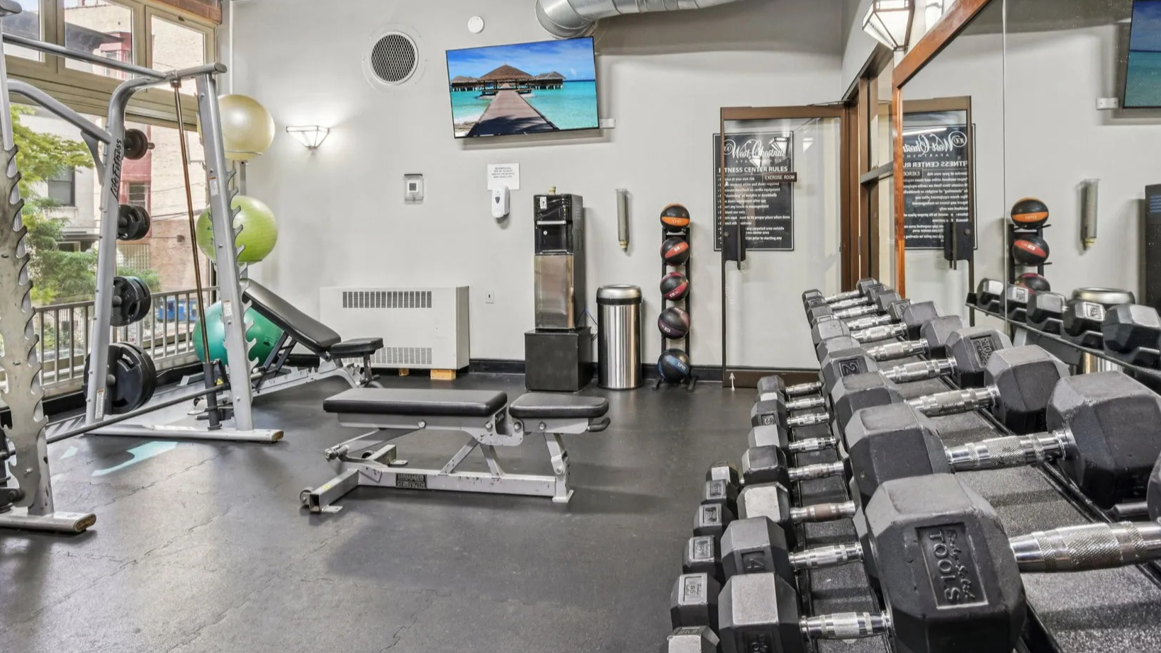 Onsite fitness center at 100 W Chestnut in Chicago offering free weights, benches, Smith machine, mirrors, and TVs for convenient daily workouts