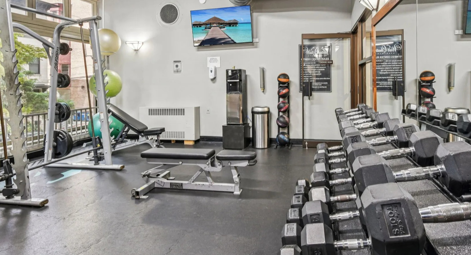 Onsite fitness center at 100 W Chestnut in Chicago offering free weights, benches, Smith machine, mirrors, and TVs for convenient daily workouts