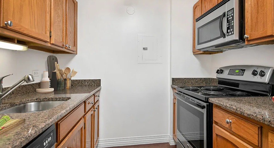 Renovated kitchen at 100 W Chestnut in Chicago with stainless steel appliances, granite countertops, wooden cabinets, and track lighting