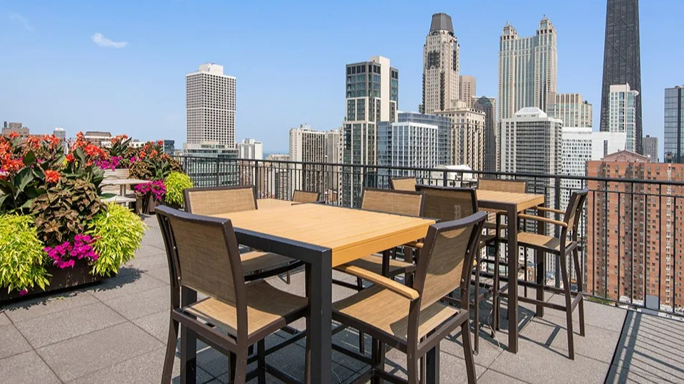 Rooftop terrace at 100 W Chestnut in Chicago with outdoor dining tables, lush planters, and panoramic views of the downtown skyline