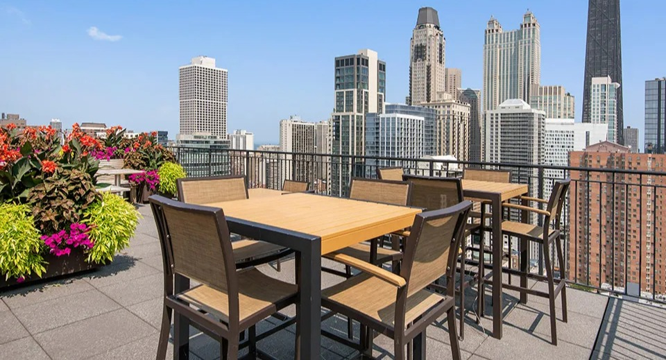 Rooftop terrace at 100 W Chestnut in Chicago with outdoor dining tables, lush planters, and panoramic views of the downtown skyline
