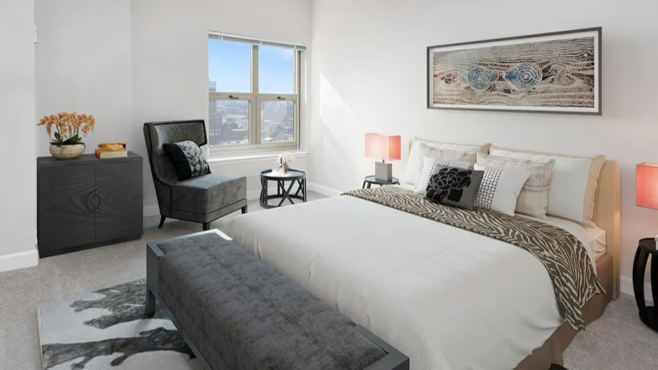 Spacious bedroom at 100 W Chestnut in Chicago with upholstered bed, stylish accent chair, neutral decor, and a large window with city views