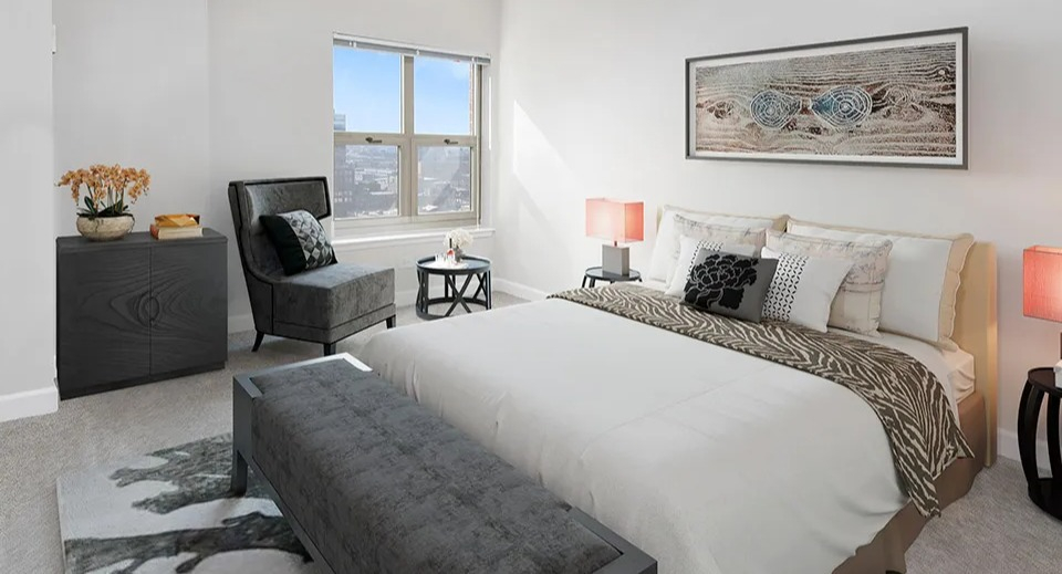 Spacious bedroom at 100 W Chestnut in Chicago with upholstered bed, stylish accent chair, neutral decor, and a large window with city views
