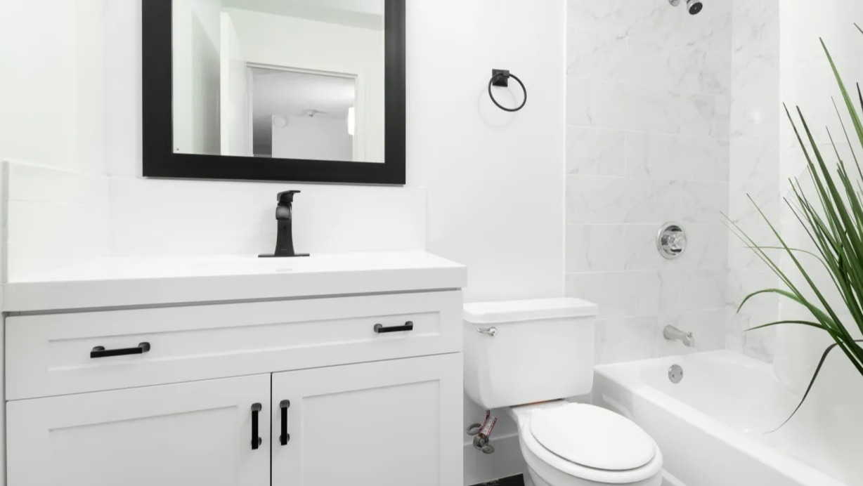 Updated bathroom at 100 W Chestnut in Chicago with white vanity, black framed mirror, modern fixtures, tiled shower, and sleek black flooring