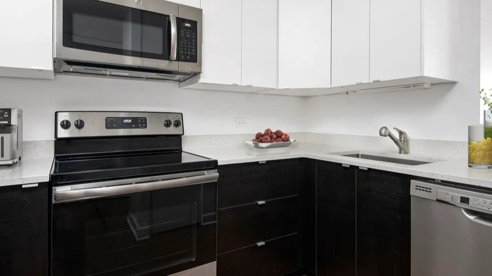 Updated kitchen at 100 W Chestnut in Chicago with stainless steel appliances, two-tone cabinets, quartz counters, and a sleek L-shaped layout
