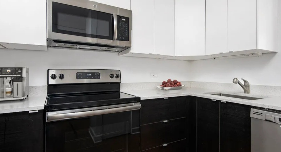 Updated kitchen at 100 W Chestnut in Chicago with stainless steel appliances, two-tone cabinets, quartz counters, and a sleek L-shaped layout