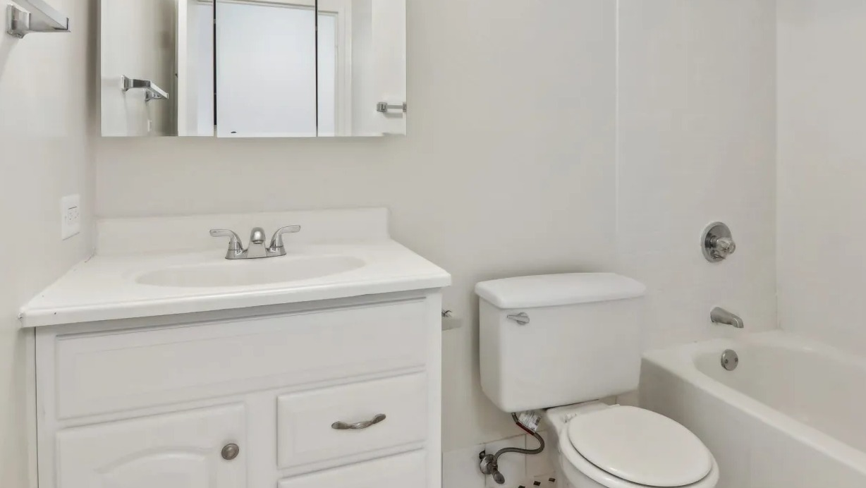 Bright bathroom at 1000 N LaSalle in Chicago featuring white vanity with mirrored cabinet, curved shower rod, and a classic tub with tiled surround