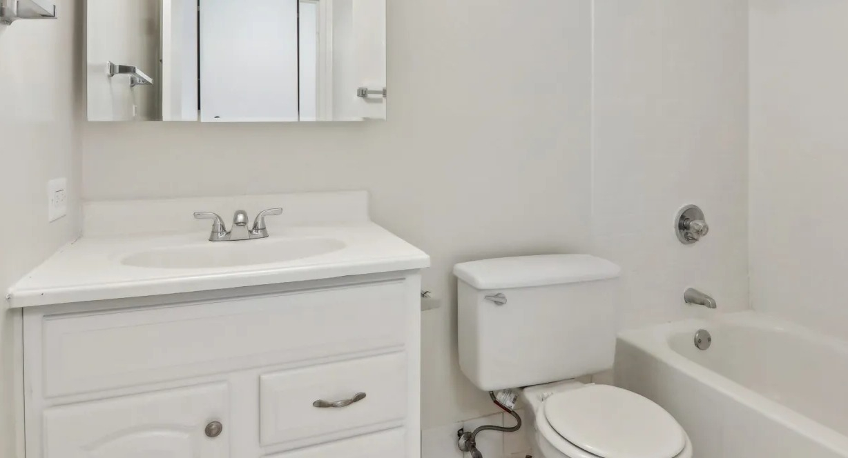 Bright bathroom at 1000 N LaSalle in Chicago featuring white vanity with mirrored cabinet, curved shower rod, and a classic tub with tiled surround