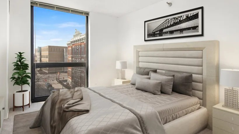 Bright bedroom with an upholstered bed, neutral bedding, nightstands, and a floor-to-ceiling window overlooking the neighborhood at 1000 N LaSalle, Chicago