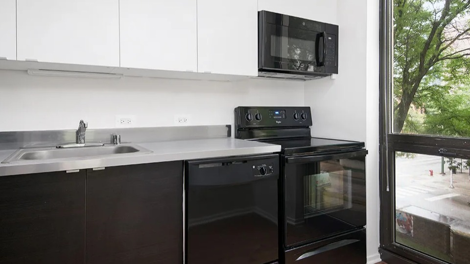 Renovated kitchen with white upper cabinets, dark base cabinets, black appliances, and a large window bringing natural light at 1000 N LaSalle apartments in Chicago