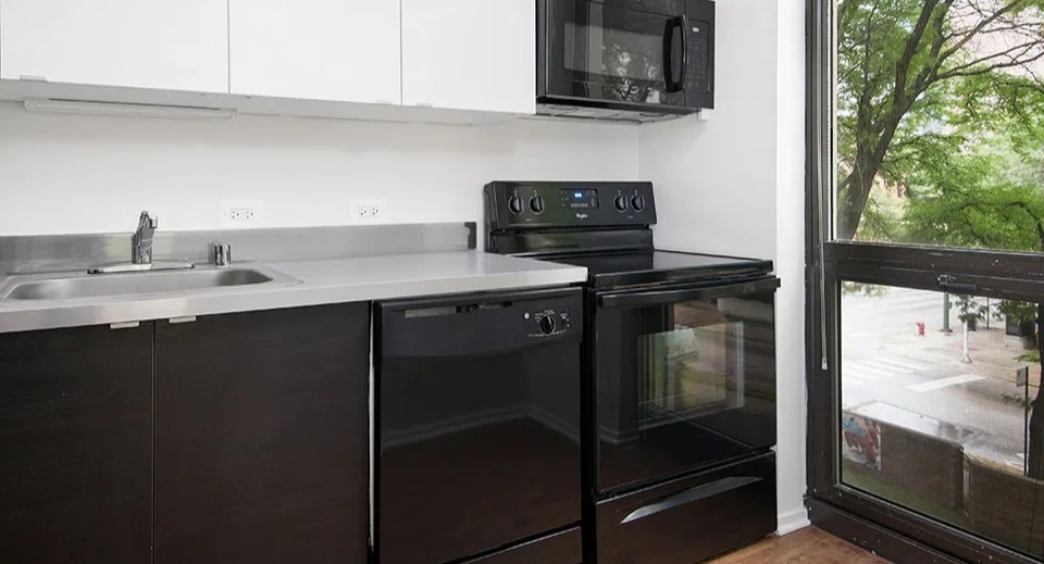Renovated kitchen with white upper cabinets, dark base cabinets, black appliances, and a large window bringing natural light at 1000 N LaSalle apartments in Chicago
