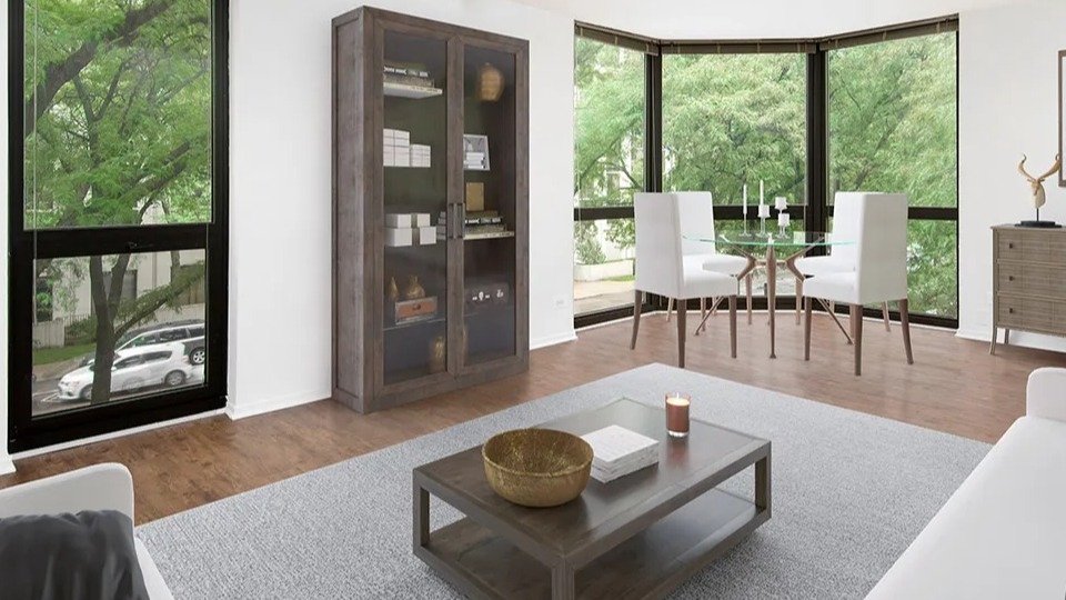 Spacious corner living room with wide bay windows, track lighting, display cabinet, and a small dining nook at 1000 N LaSalle apartments in Chicago