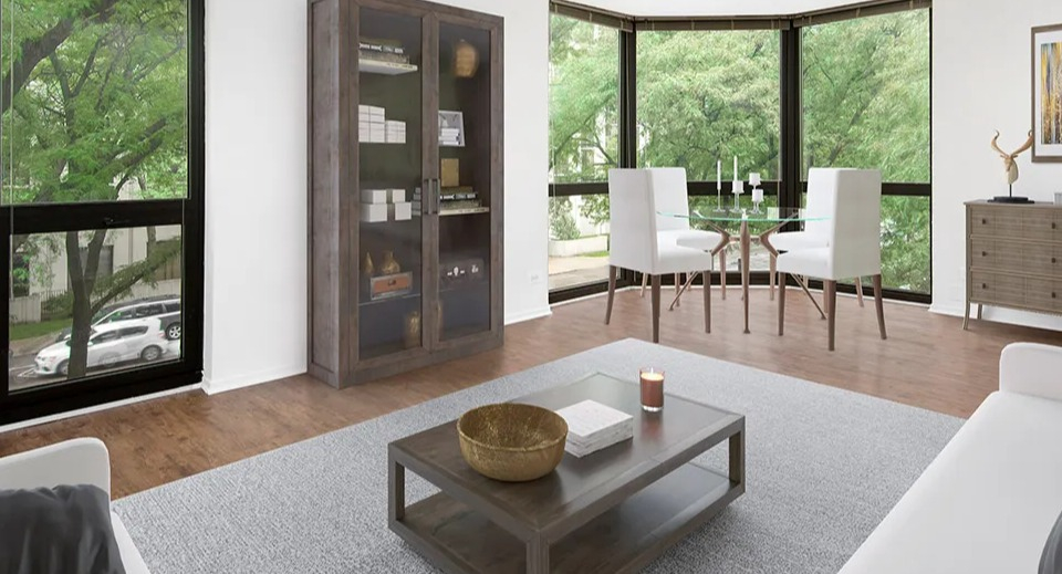 Spacious corner living room with wide bay windows, track lighting, display cabinet, and a small dining nook at 1000 N LaSalle apartments in Chicago