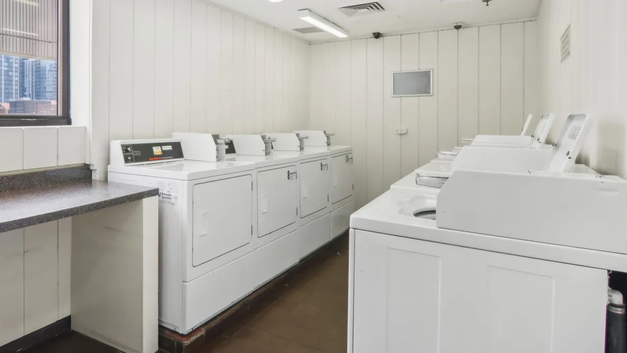 On-site laundry room at 1000 N LaSalle in Chicago with top-loading washers, dryers, folding counter, bright lighting, and a window offering city views