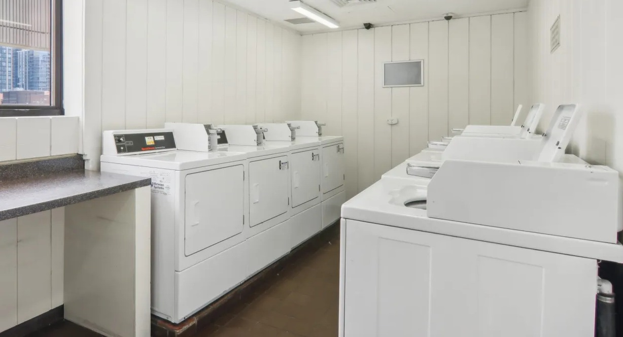 On-site laundry room at 1000 N LaSalle in Chicago with top-loading washers, dryers, folding counter, bright lighting, and a window offering city views