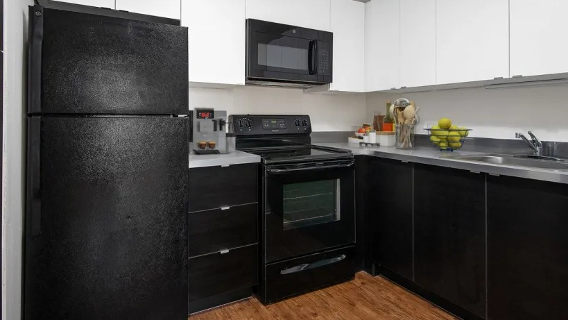 Updated kitchen with white upper cabinets, dark base cabinets, stainless countertop, and black appliances at 1000 N LaSalle apartments in Chicago