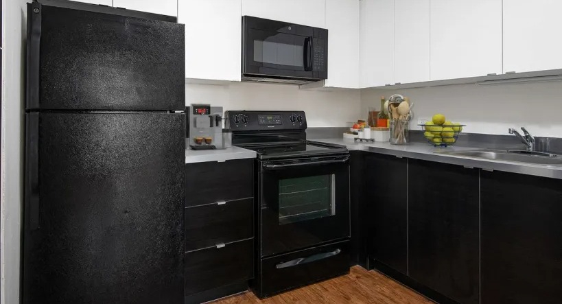Updated kitchen with white upper cabinets, dark base cabinets, stainless countertop, and black appliances at 1000 N LaSalle apartments in Chicago
