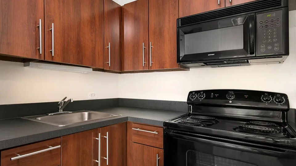 U-shaped kitchen with rich wood cabinets, dark countertops, black appliances, and a stainless sink at 1000 N LaSalle apartments in Chicago