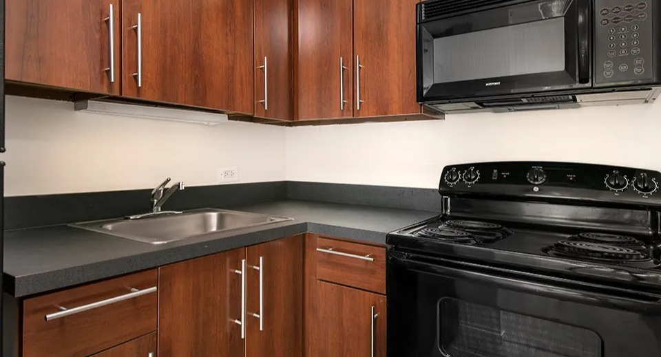 U-shaped kitchen with rich wood cabinets, dark countertops, black appliances, and a stainless sink at 1000 N LaSalle apartments in Chicago