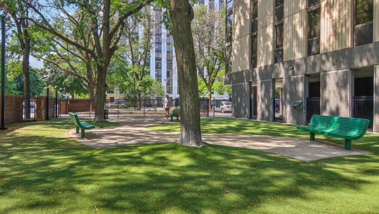 Shaded outdoor courtyard at 1000 N LaSalle in Chicago featuring fenced green space, mature trees, and benches for relaxing in the Gold Coast