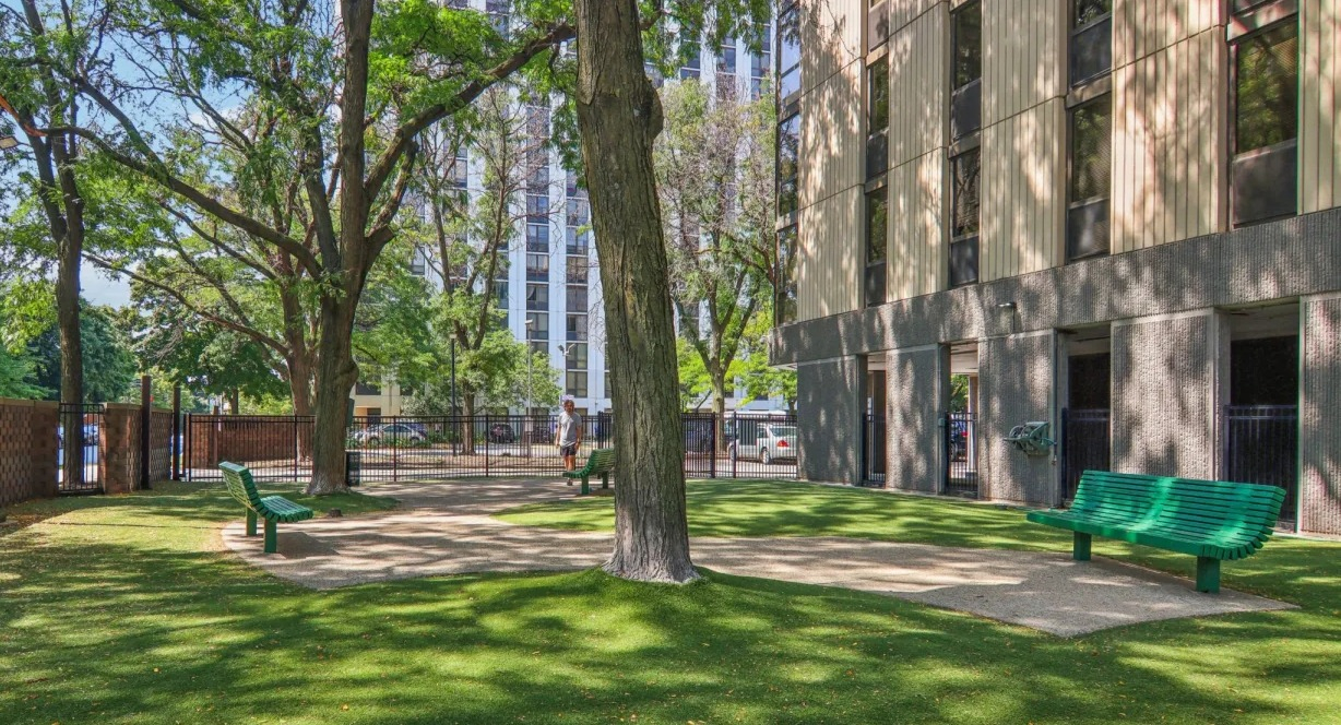 Shaded outdoor courtyard at 1000 N LaSalle in Chicago featuring fenced green space, mature trees, and benches for relaxing in the Gold Coast