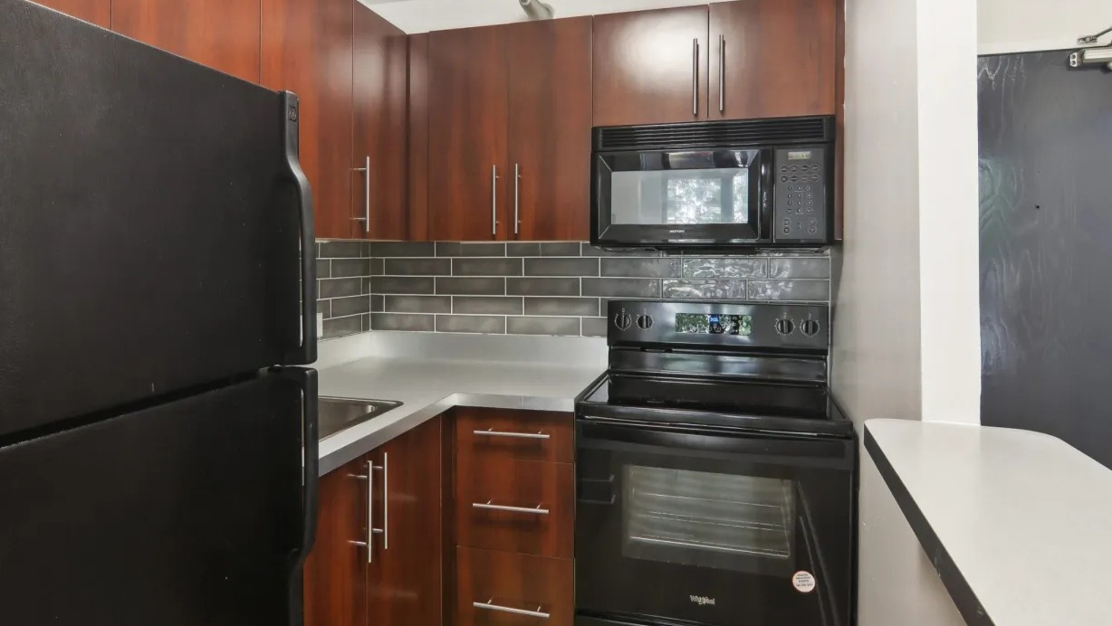 Renovated kitchen at 1000 N LaSalle in Chicago with warm wood cabinetry, dark appliances, subway tile backsplash, and a compact L-shaped layout