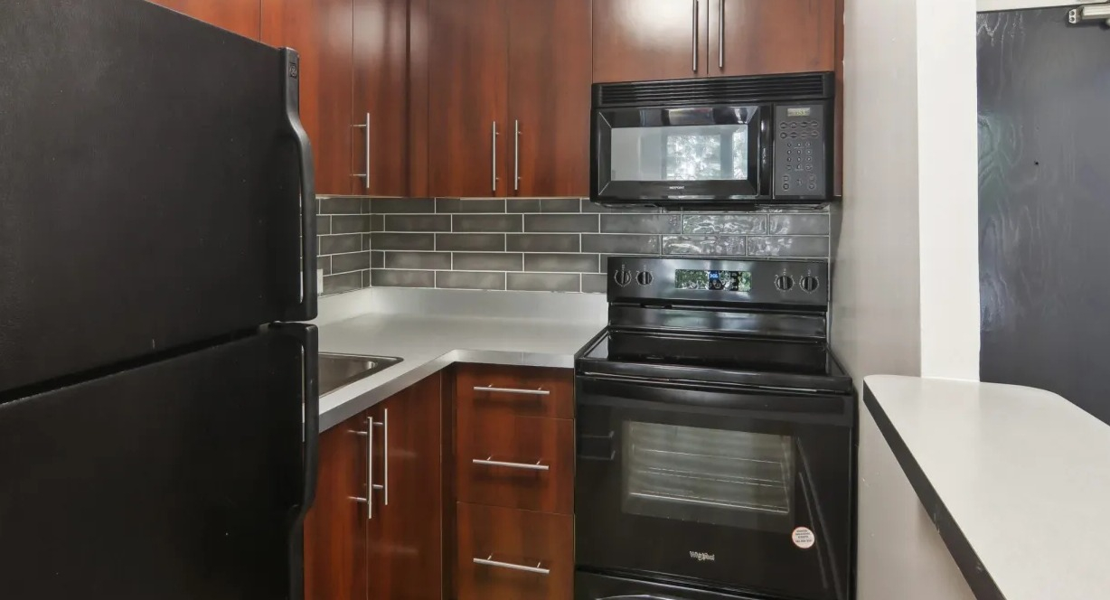 Renovated kitchen at 1000 N LaSalle in Chicago with warm wood cabinetry, dark appliances, subway tile backsplash, and a compact L-shaped layout