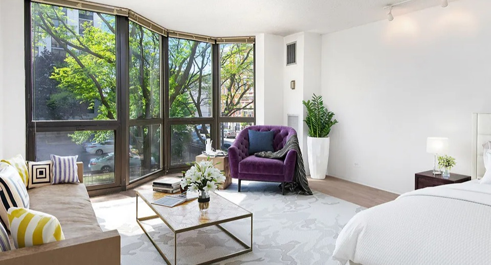 Large studio layout with bed, seating area, and expansive bay windows that fill the open space with light at 1000 N LaSalle apartments in Chicago