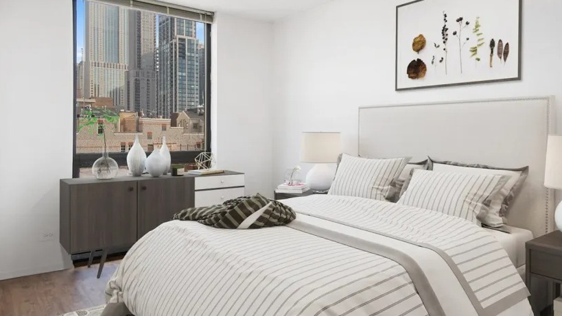 Updated bedroom at 1000 N LaSalle in Chicago with queen bed, striped bedding, wood floors, large window, and skyline city views