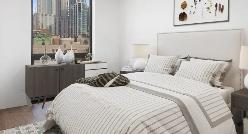 Updated bedroom at 1000 N LaSalle in Chicago with queen bed, striped bedding, wood floors, large window, and skyline city views