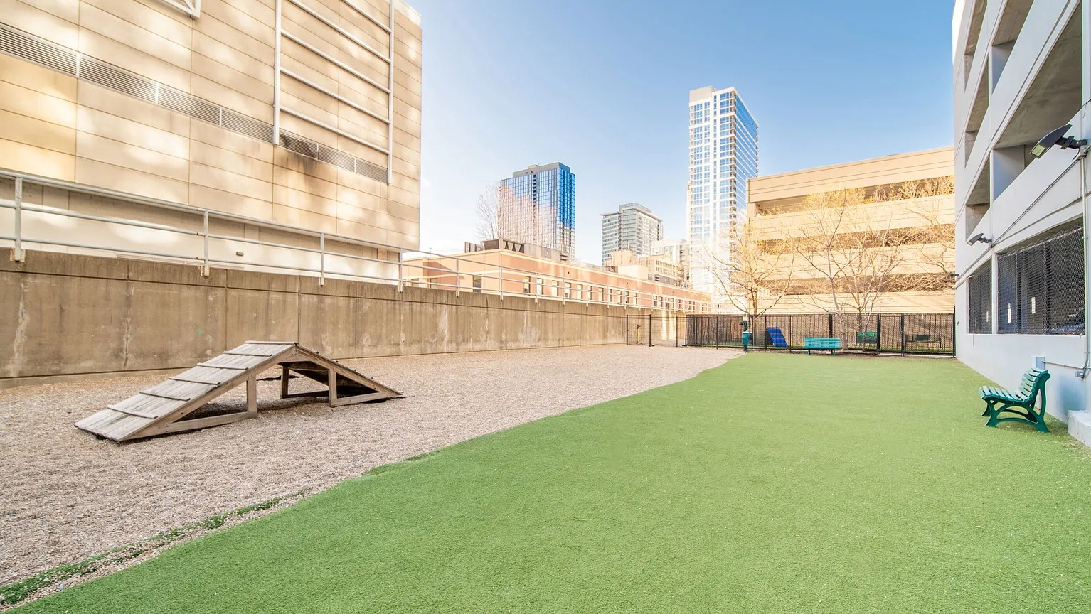 Outdoor dog park with agility ramp, green turf, and city views providing pet-friendly amenities at 1000 South Clark apartments in Chicago