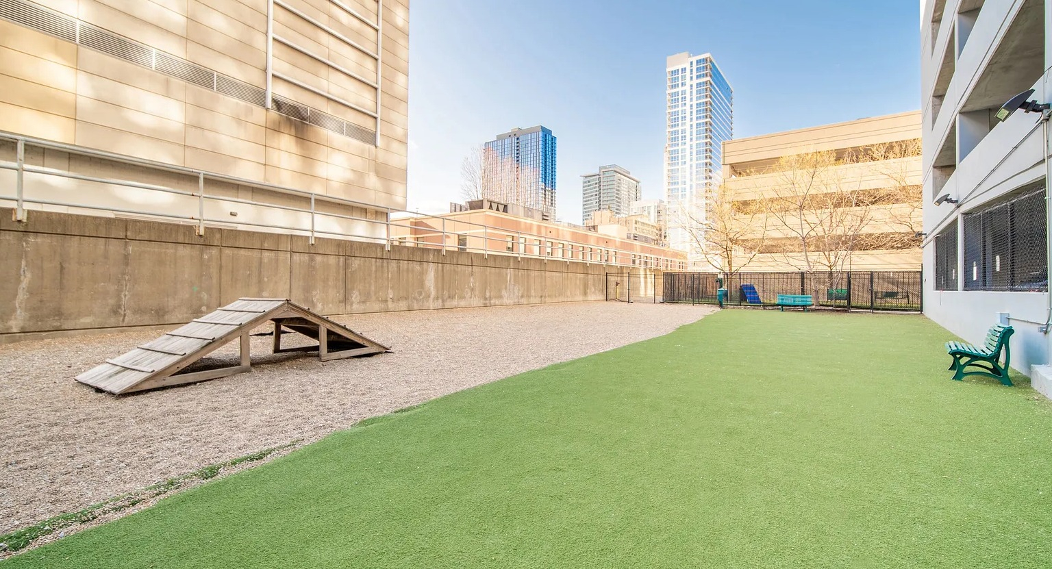Outdoor dog park with agility ramp, green turf, and city views providing pet-friendly amenities at 1000 South Clark apartments in Chicago