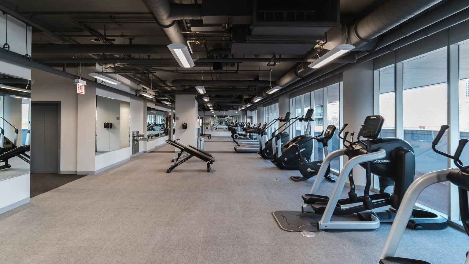 Spacious fitness center with treadmills, ellipticals, weight benches, mirrors, and window light at 1000 South Clark apartments in Chicago
