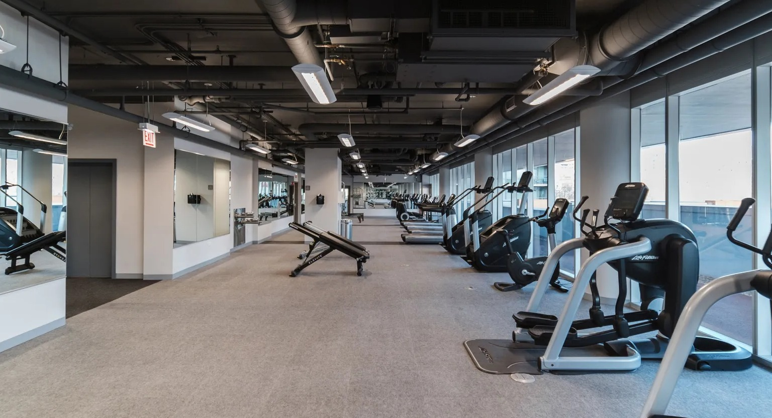 Spacious fitness center with treadmills, ellipticals, weight benches, mirrors, and window light at 1000 South Clark apartments in Chicago