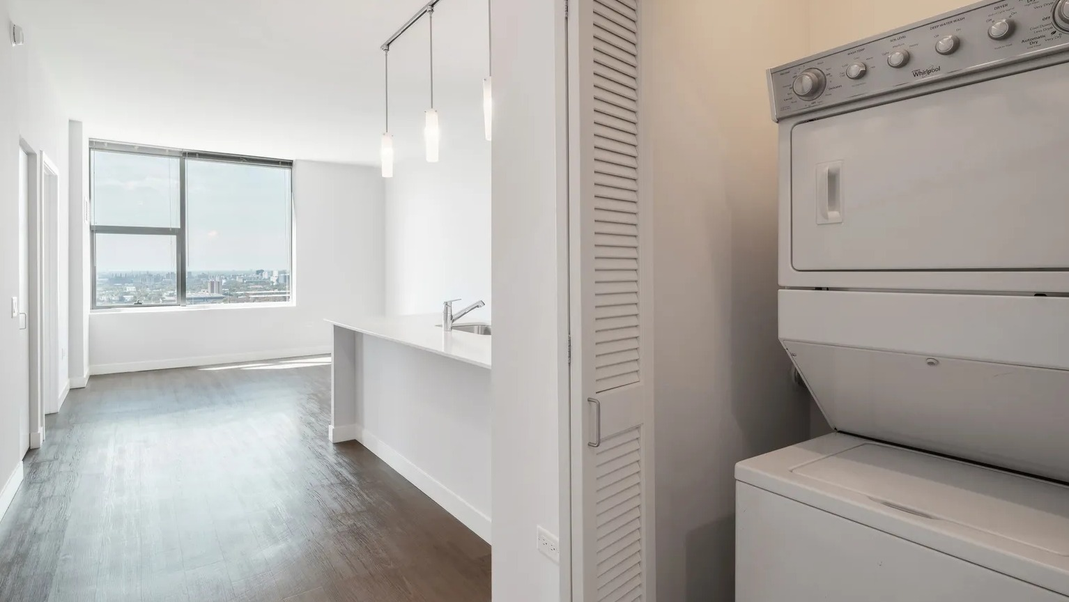 In-unit stacked washer and dryer located in hallway closet near kitchen, providing convenience at 1000 South Clark apartments in Chicago