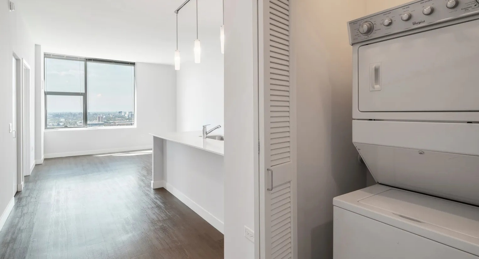 In-unit stacked washer and dryer located in hallway closet near kitchen, providing convenience at 1000 South Clark apartments in Chicago