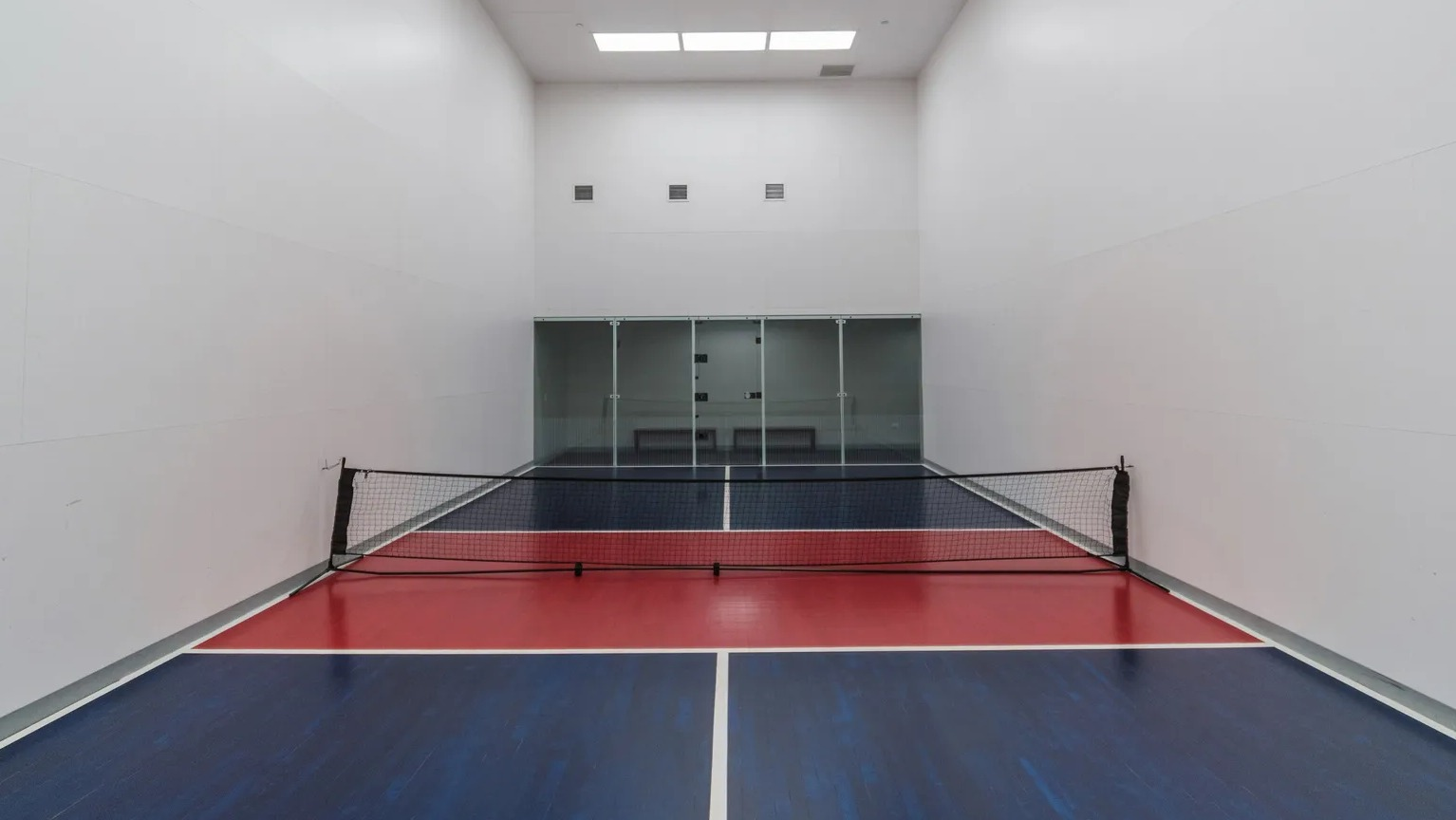 Indoor multi-sport court with pickleball net, bright overhead lighting, and glass back wall at 1000 South Clark apartments in Chicago