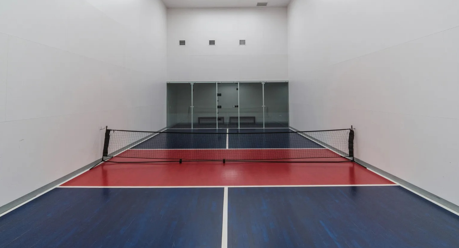 Indoor multi-sport court with pickleball net, bright overhead lighting, and glass back wall at 1000 South Clark apartments in Chicago